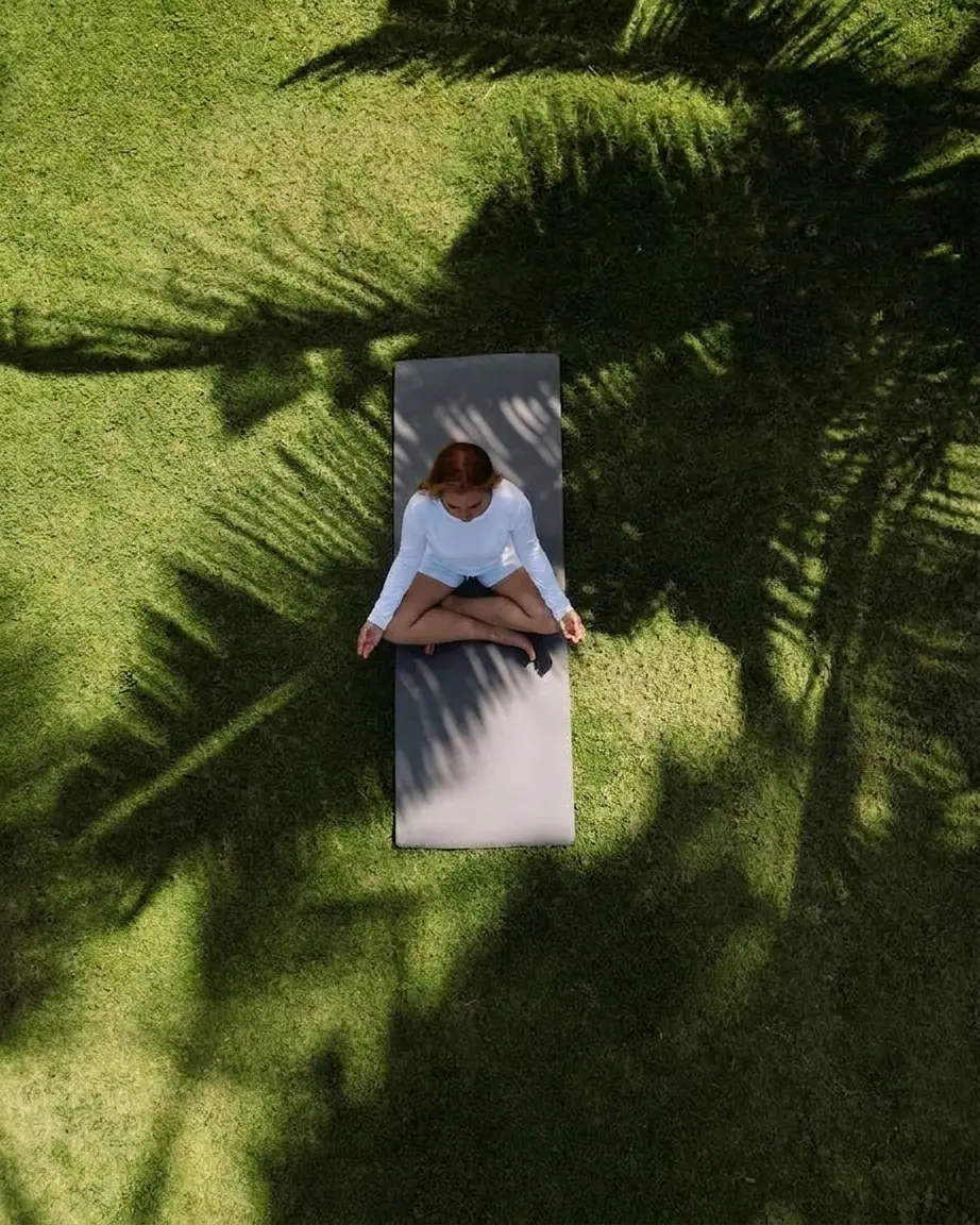 Femme assise en méditation sur un tapis posé dans l'herbe, vue du dessus